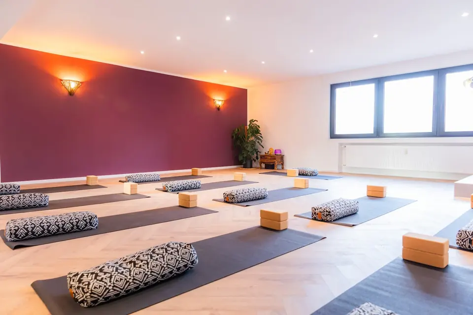 Heller Yogaraum mit ausgelegten Matten, Bolstern und beerenfarbener Wand