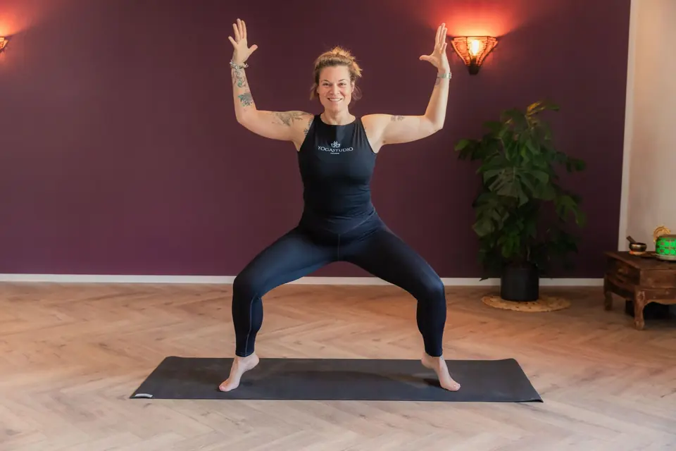 Frau in einer kraftvollen Standhaltung mit erhobenen Armen im Yogaraum