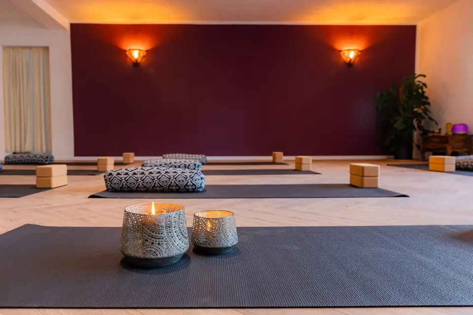 Yogaraum mit Matten, Sitzkissen und Pflanzen vor der beerenfarbenen Wand