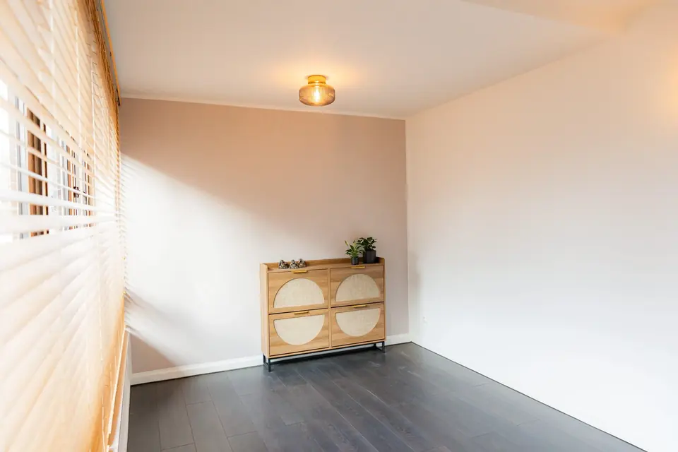 Kleiner Raum mit dunklem Boden, Kommode und Fenster mit Jalousie
