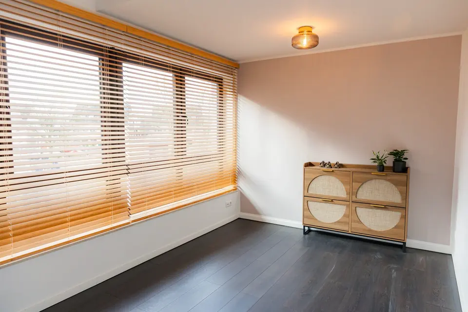 Kleiner Raum mit Fensterfront, Jalousien und Kommode