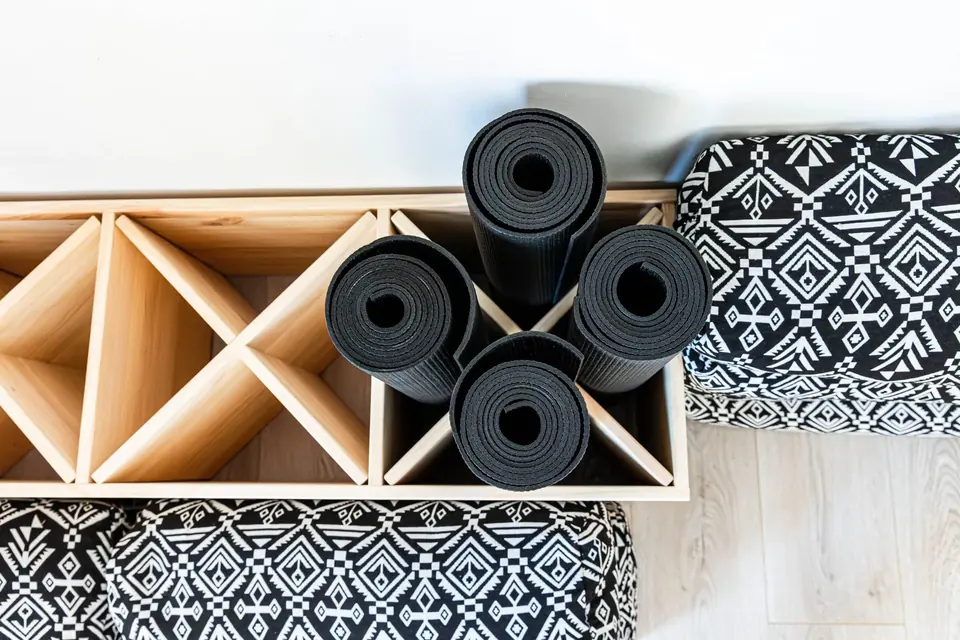 Gerollte Yogamatten und gemusterte Bolster im Holzregal, von oben fotografiert