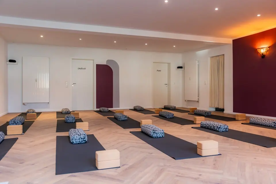 Großer Yogaraum mit ausgelegten Matten, Kissen und Blöcken vor der beerenfarbenen Wand